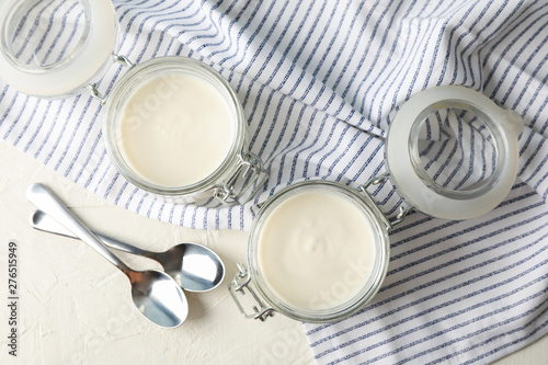 Glass jars with sour cream yogurt, spoons and towel on white cement background