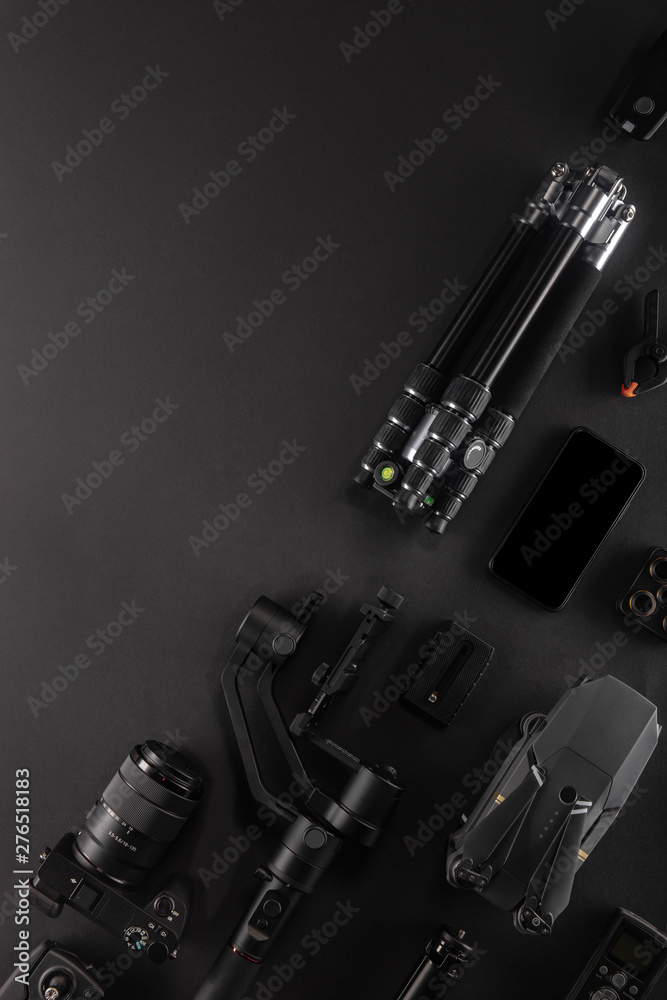 Work space videographer with laptop, digital camera, memory card, action camera, drone, remote controller, phone and camera accessory. Top view on black table background. Concept of mockup template. Work space videographer with laptop, digital camera, memory card, action camera, drone, remote controller, phone and camera accessory. Top view on black table background. Concept of mockup template.