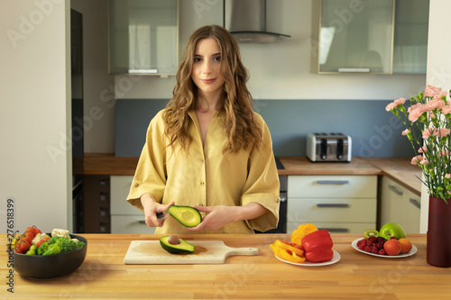 Young beautiful girl slices ripe avocado. A woman prepares a salad of fresh  healthy vegetables.