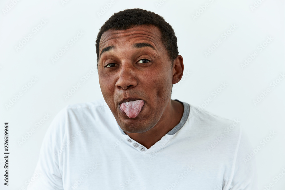 Fototapeta premium Making face,funny foolishes portrait of African American man showing him tongue against white background.