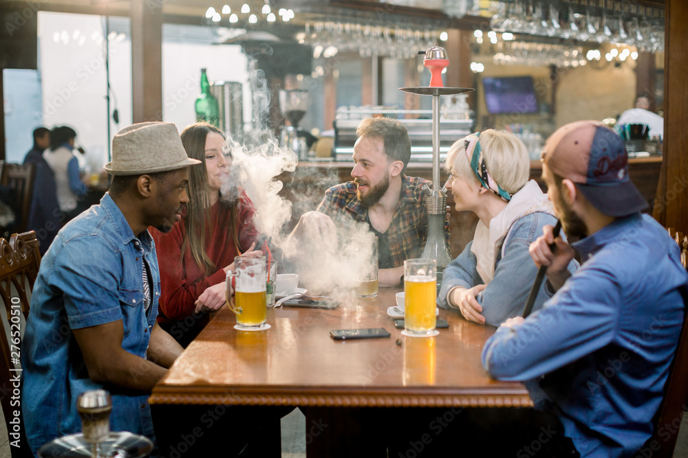 Young multiracial people vapor hookah pipe in shisha bar lounge