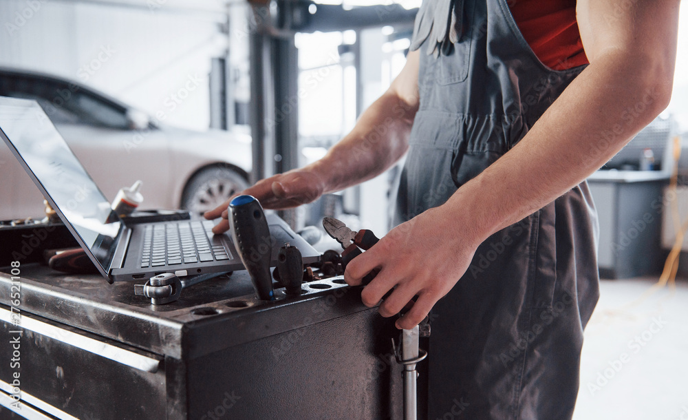 Working hands. Man indoors in uniform using laptop for his job for fixing broken car Working hands. Man indoors in uniform using laptop for his job for fixing broken car