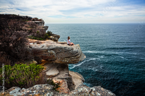 Photography Relaxed woman sitting on coastal headland looking out to ocean