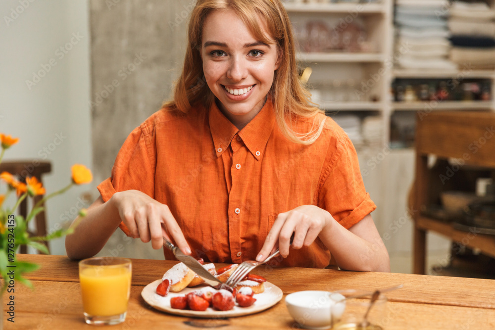 Happy young blonde girl at the kitchen eat sweet pastry have a breakfast drinking juice.