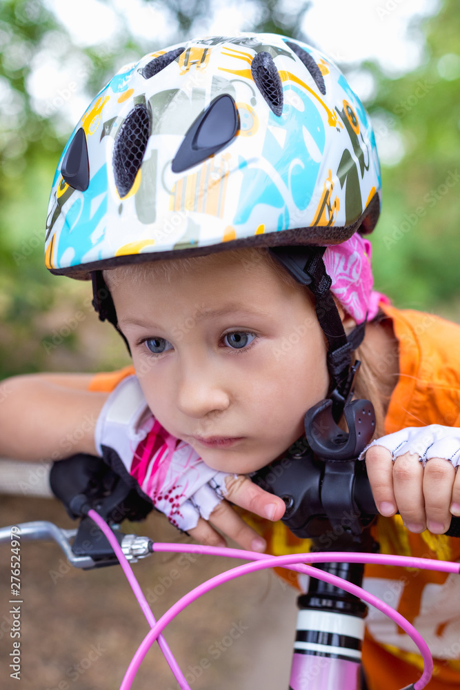 Cute little sad girl in a helmet with a bike in the summer