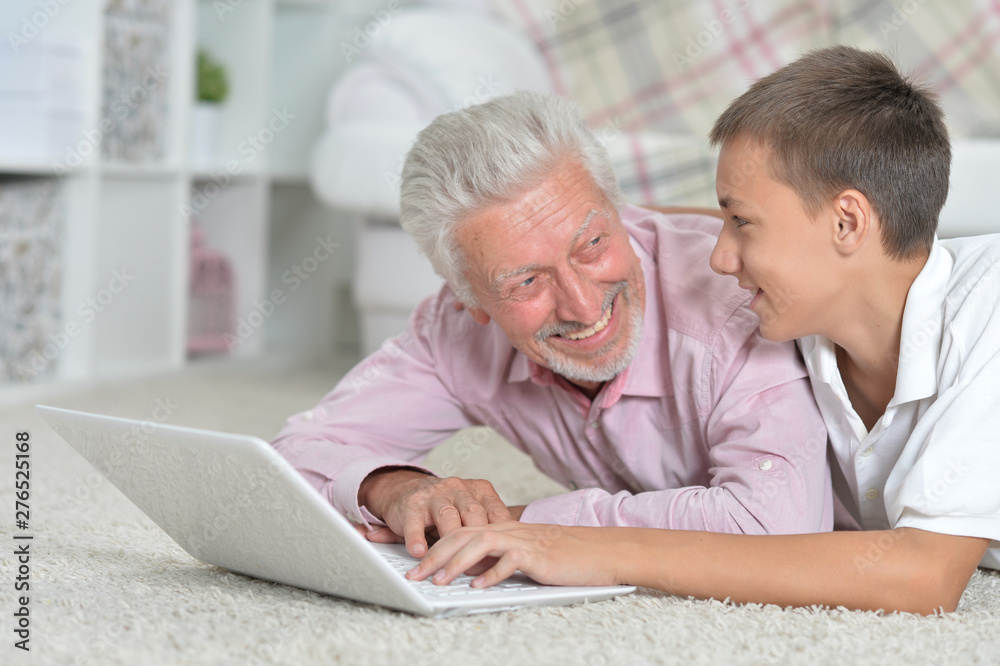 Obraz premium Grandfather with grandson using laptop while lying on floor