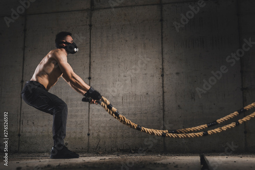 Muscular man exercising with battle ropes