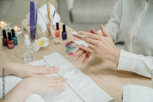 Woman manicurist removing lacquer from manicured nails with white cotton pad on customer hands. focus photo of two asian female hands in home call service. nail specialist clean up client finger