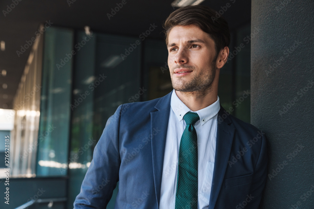 Fototapeta premium Concentrated serious young unshaved handsome business man outdoors at the street near business center posing looking aside.