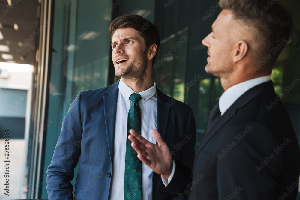 Image of irritated businessmen partners talking and discussing conflict while standing outside office center