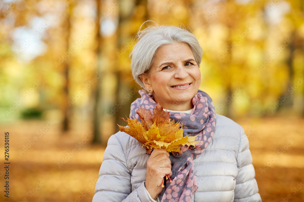 old age, retirement and season concept - portrait of happy senior woman with maple leaves at autumn park