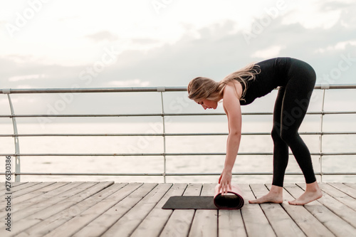 Woman rolls yoga mat before asana training at the sea on sunrise