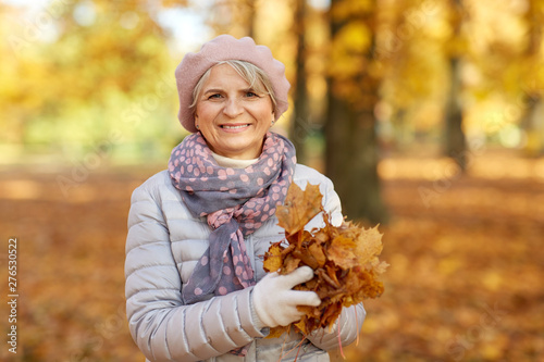 old age  retirement and season concept - portrait of happy senior woman with maple leaves at autumn park