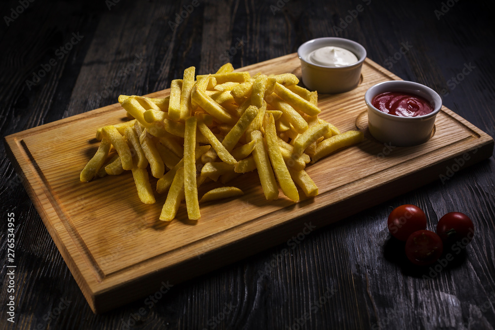 Delicious french fries with sauce on wooden cutting board on wooden table in low key Delicious french fries with sauce on wooden cutting board on wooden table in low key