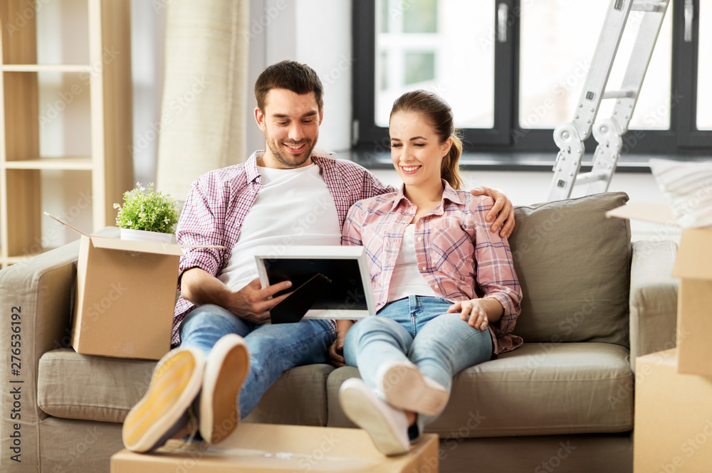 moving, people, repair and real estate concept - happy couple with photo frame and cardboard boxes sitting on sofa at new home