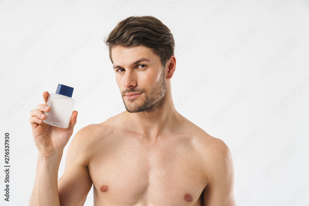 Photo closeup of young naked man looking at camera and holding aftershave lotion Photo closeup of young naked man looking at camera and holding aftershave lotion