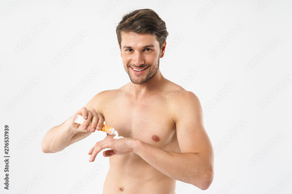 Photo closeup of young naked man smiling at camera and applying hand cream Photo closeup of young naked man smiling at camera and applying hand cream
