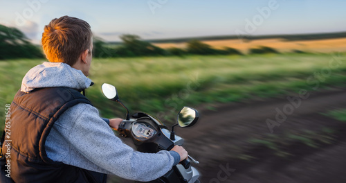 Riding along an empty road in the forest against the sunset sky. Scooter steering wheel and speedometer closeup. The concept of freedom, high speed and travel in nature, banner.