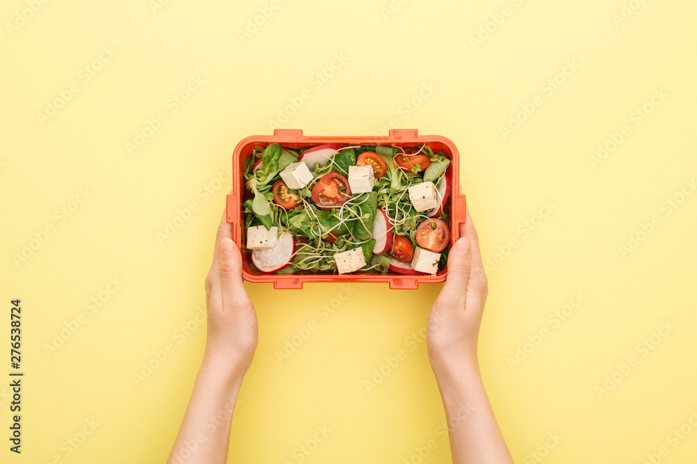 cropped view of woman holding lunch box with salad in hands on yellow background