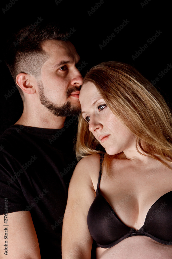 a man and a pregnant woman couple in their ninth month of pregnancy are embracing against an isolated black background. waiting for replenishment in the family a man and a pregnant woman couple in their ninth month of pregnancy are embracing against an isolated black background. waiting for replenishment in the family
