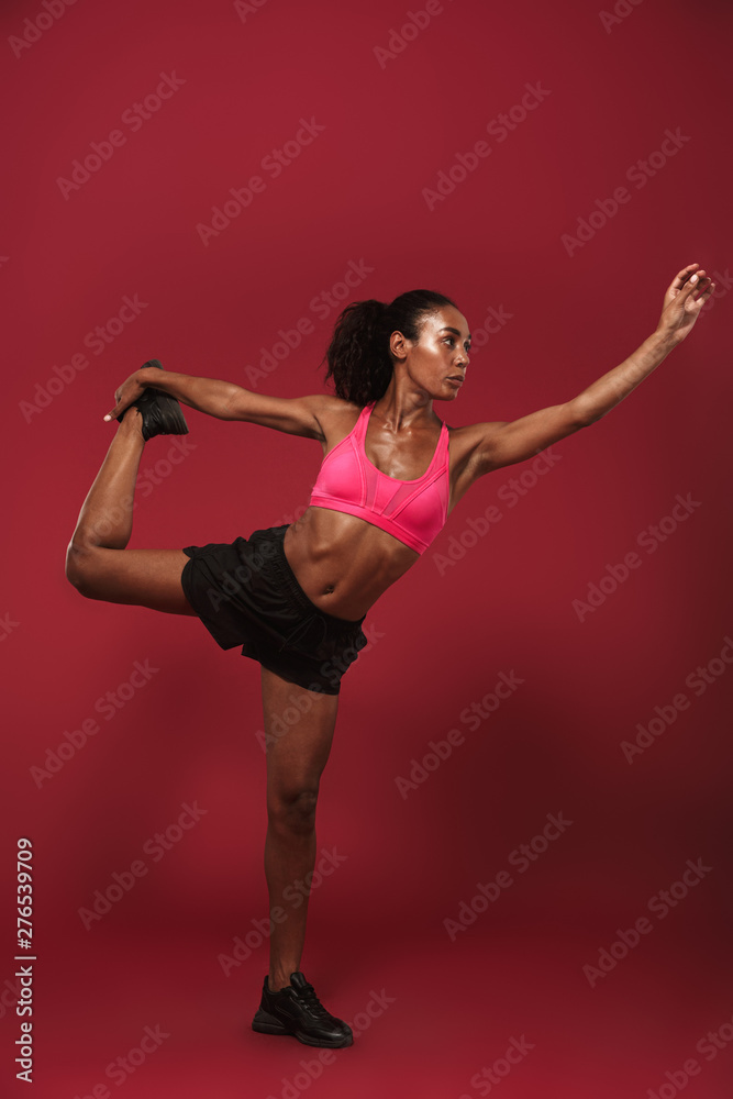 Beautiful concentrated strong young african sports woman posing isolated over red wall background make yoga exercise.