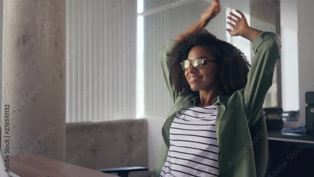 Young woman sitting at desk in front of laptop stretching her arms