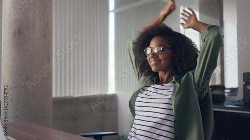 Young woman sitting at desk in front of laptop stretching her arms