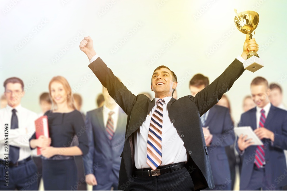 Happy businessman with golden cup celebrating win with businesspeople on background Happy businessman with golden cup celebrating win with businesspeople on background