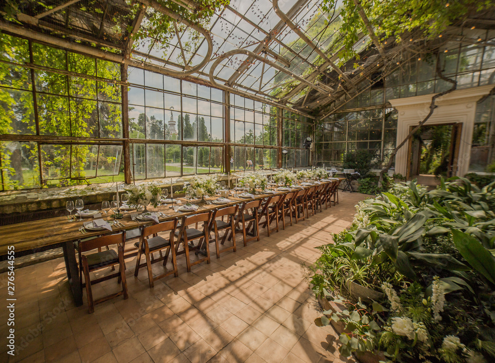 A large glass room with greenery throughout the area decorated by a banquet on a certified table with flower arrangements