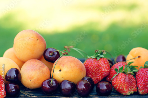 Juicy summer fruits and berries - apricots, cherries and strawberries lie in close-up against the background of a green lawn