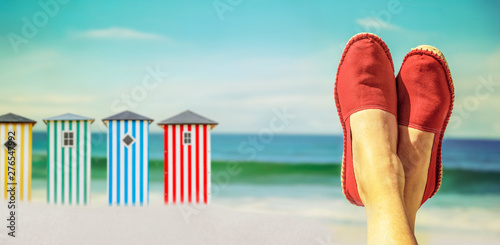 Beine mit roten Stoffschuhen vor Strand und Meer