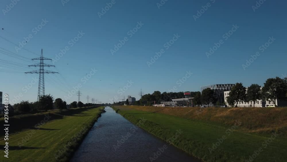 Sliding reveal shot of a small water stream river surrounded by grass and trees under the buke skies from behind the bridge railings in Offenburg, Germany Sliding reveal shot of a small water stream river surrounded by grass and trees under the buke skies from behind the bridge railings in Offenburg, Germany