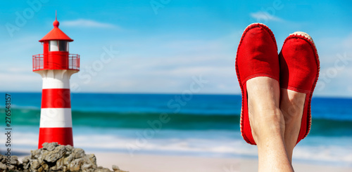 Beine mit roten Stoffschuhen vor Strand und Meer