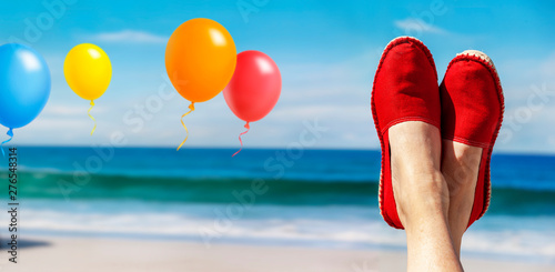Beine mit roten Stoffschuhen vor Strand und Meer