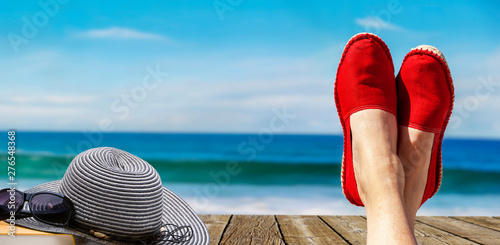 Beine mit roten Stoffschuhen vor Strand und Meer
