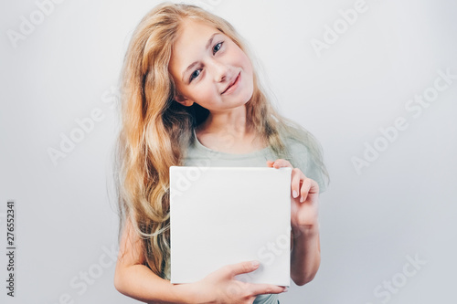 Beautiful girl with blank canvas board for message or photo. Copy space. Cute teen caucasian girl with blond hair holding in her hands mockup poster and standing against grey wall.