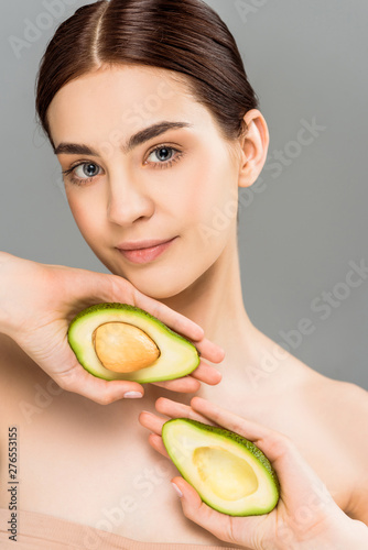 beautiful young woman holding avocado halves isolated on grey