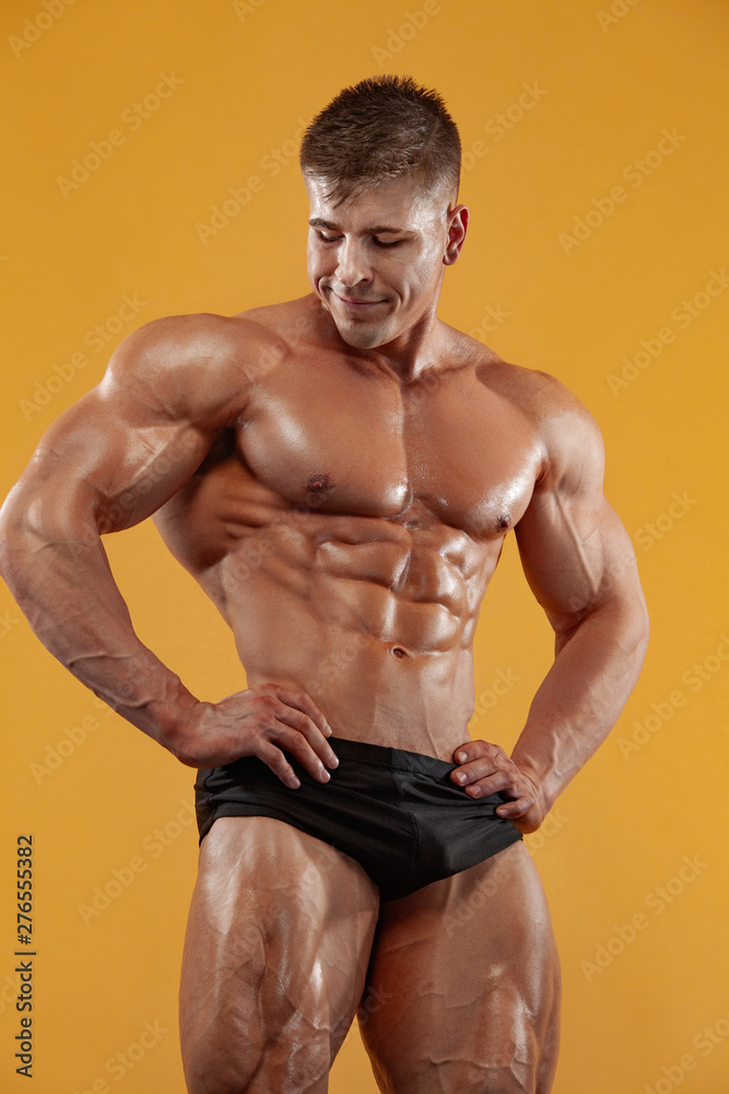 Brutal strong muscular bodybuilder athlete man pumping up muscles on yellow background. Workout bodybuilding concept.