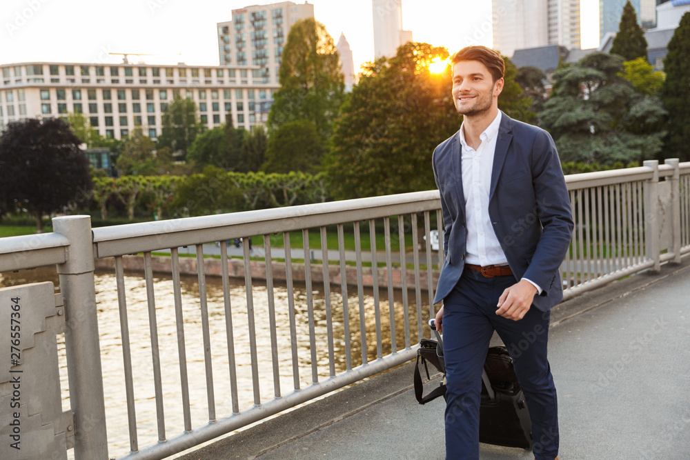Happy businessman walking outdoors on the street with suitcase with beautiful sunlight. Happy businessman walking outdoors on the street with suitcase with beautiful sunlight.