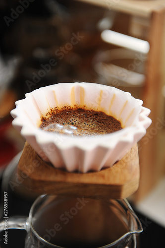 Blooming coffee in pink ceramic origami dripper. On wooden coffee stand. Close up. Alternative manual brewing