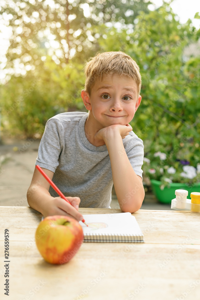 Fototapeta premium Cute boy draws with pencils still life. Open air. Garden in the background. Creative concept.