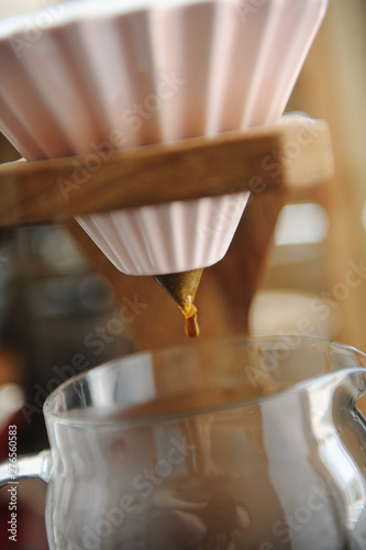 Close up coffee dripping. Alternative brewing in pink ceramic origami dripper on wooden stand.