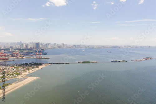 Port in Manila, Philippines. Sea port with cargo cranes. Cityscape with poor areas and business center in the distance, view from above. Asian metropolis.