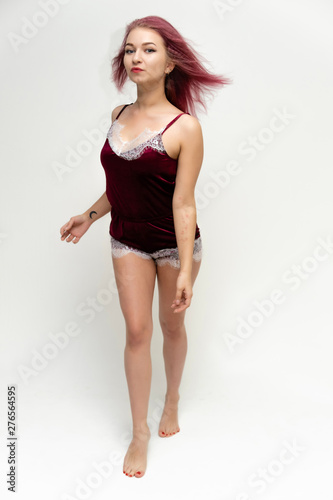 Concept portrait of a full-length pretty sexy girl with purple hair in beautiful red lingerie on a white background. She smiles, happy with life, happy. Hair flying, front view. Made in a studio.