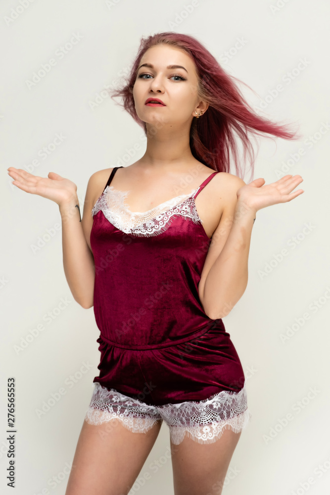Concept portrait of a knee-high pretty sexy girl with purple hair in beautiful red lingerie on a white background. She smiles, happy with life, happy. Hair flying, front view. Made in a studio.