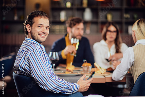 Young arab man dressed smart casual sitting at dinner in restaurant and using smart phone.