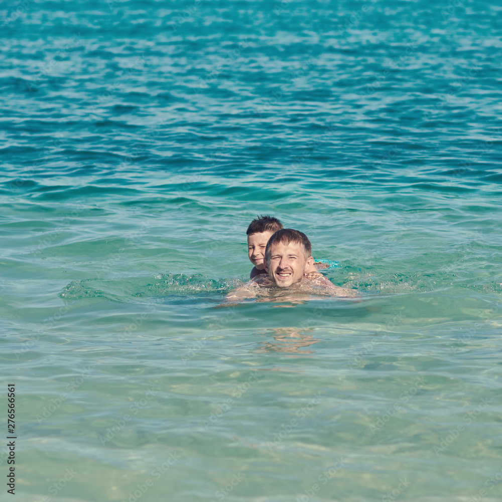 European man is happy to spend his summer holidays with his son. They are swimming in the ocean and enjoying pastime.
