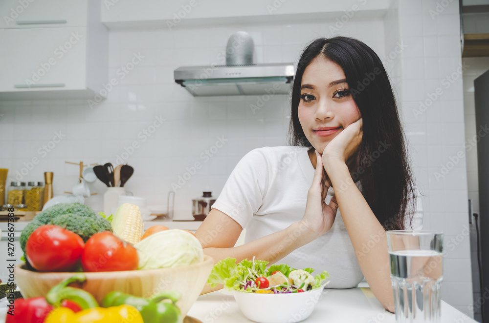 Dieting. beautiful young woman slim body in white shirt looking at camera with healthy food, fresh vegetable salad sitting in kitchen interior in house, lifestyle, good healthy and diet food concept Dieting. beautiful young woman slim body in white shirt looking at camera with healthy food, fresh vegetable salad sitting in kitchen interior in house, lifestyle, good healthy and diet food concept