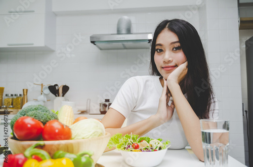 Dieting. beautiful young woman slim body in white shirt looking at camera with healthy food  fresh vegetable salad sitting in kitchen interior in house  lifestyle  good healthy and diet food concept