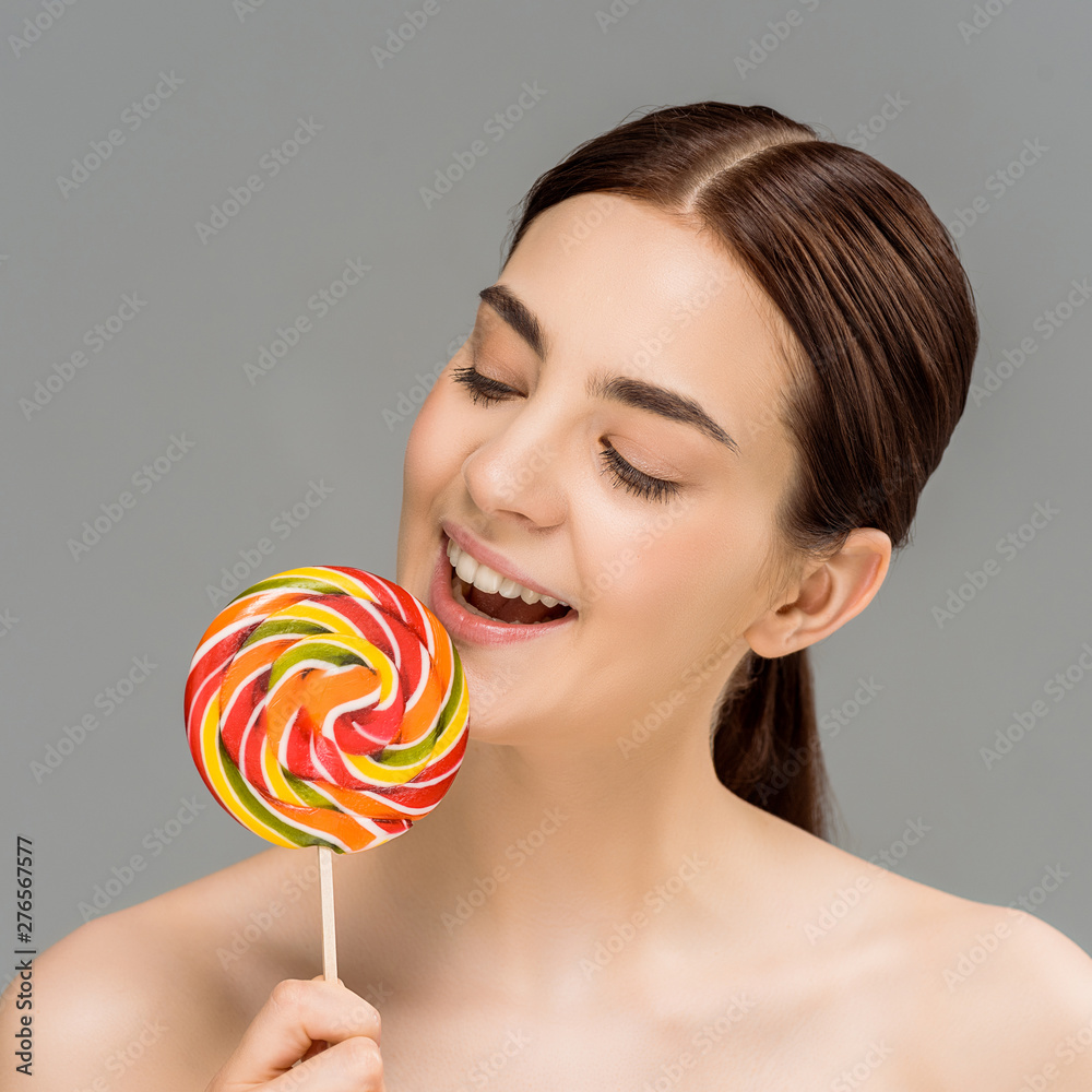 cheerful naked woman looking at colorful lollipop isolated on grey